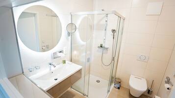 A modern bathroom with a glass-enclosed shower, a round mirror, and a white sink.
