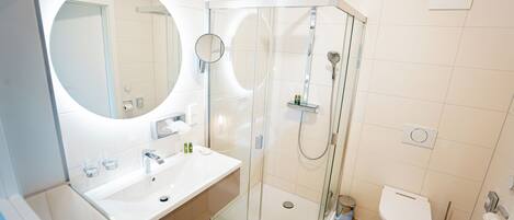 Un baño moderno con ducha de vidrio, espejo redondo y lavamanos blanco.