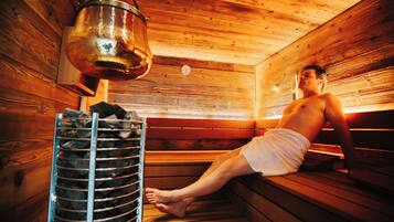 A sauna with wooden benches, a metal heater, and a person sitting on one of the benches.