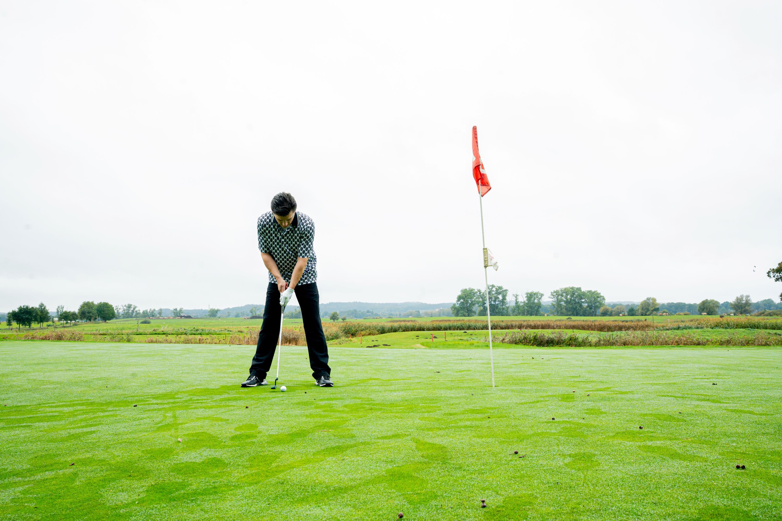 Eine Person auf einem Golfplatz, im Hintergrund ein Fahnenstange.