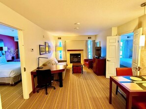 Quarto de hotel com cama, escrivaninha, televisão, lareira e área de jantar.