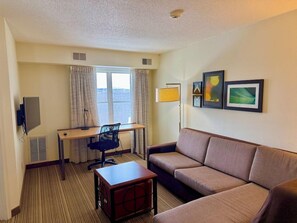 A hotel room with a sofa, a desk, a chair, a television, and framed artwork on the wall. - Residence Inn by Marriott Madison East (Madison)