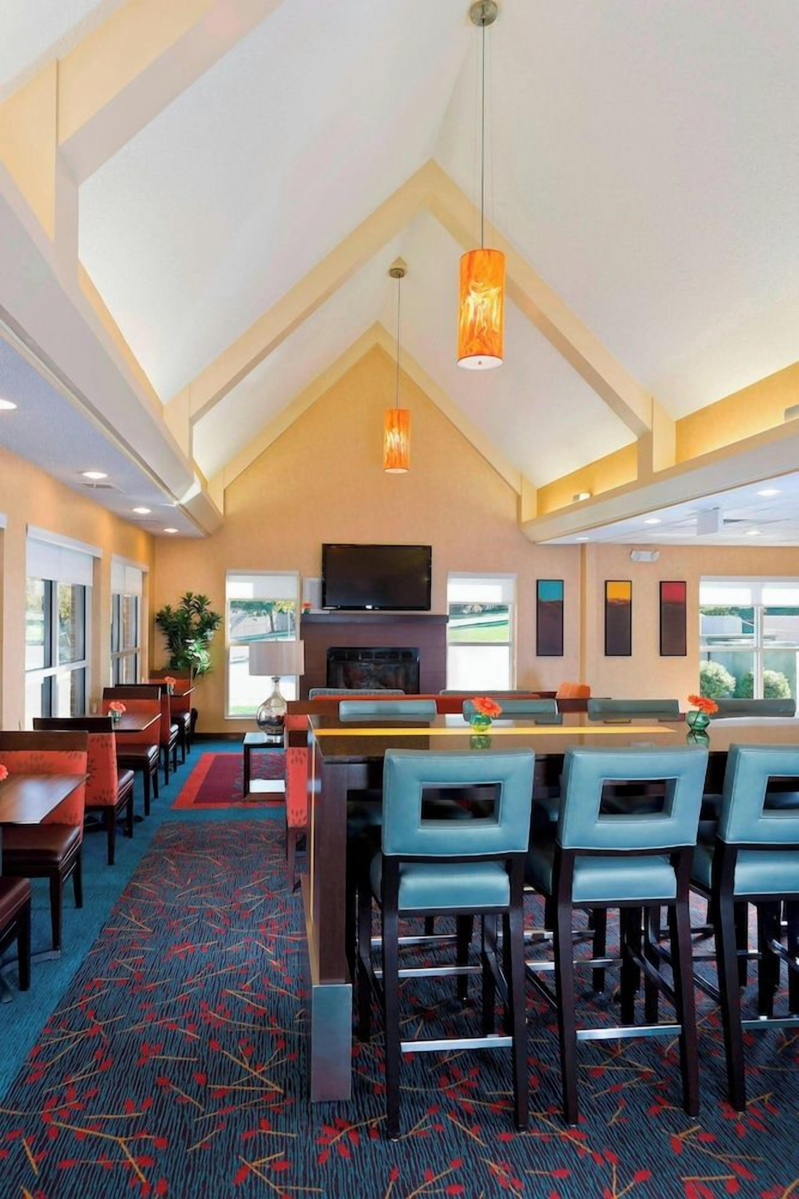 A hotel lobby with a high ceiling, a bar area, seating arrangements, and a television mounted on the wall.