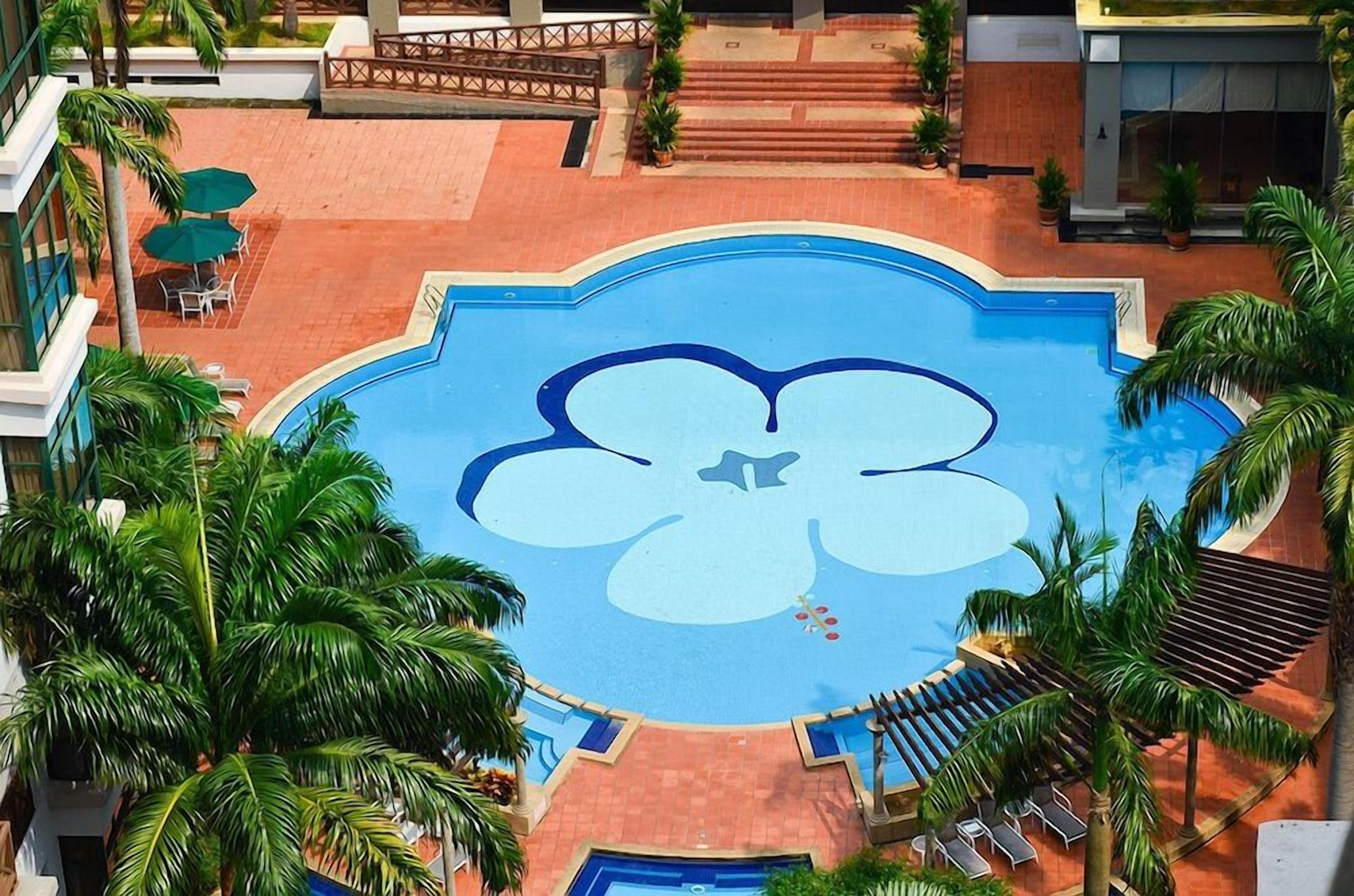 Une piscine décorée de motifs floraux, entourée de palmiers et de chaises longues.