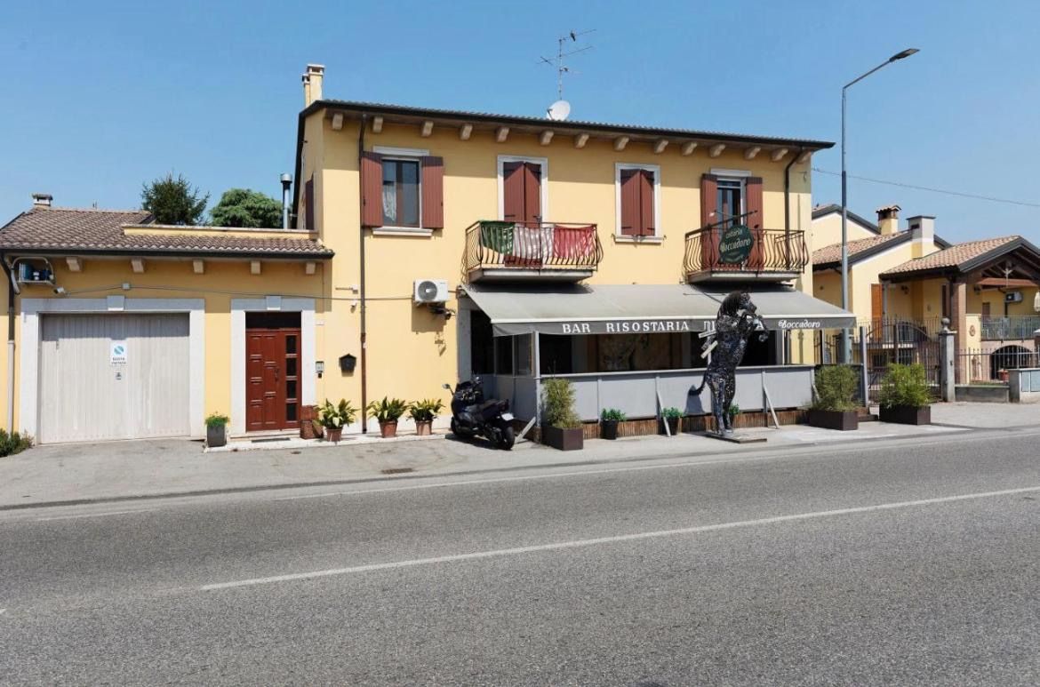 A building with a bar named 'BAR RISOSTARIA' on the ground floor, a balcony with plants, and a parked motorcycle.