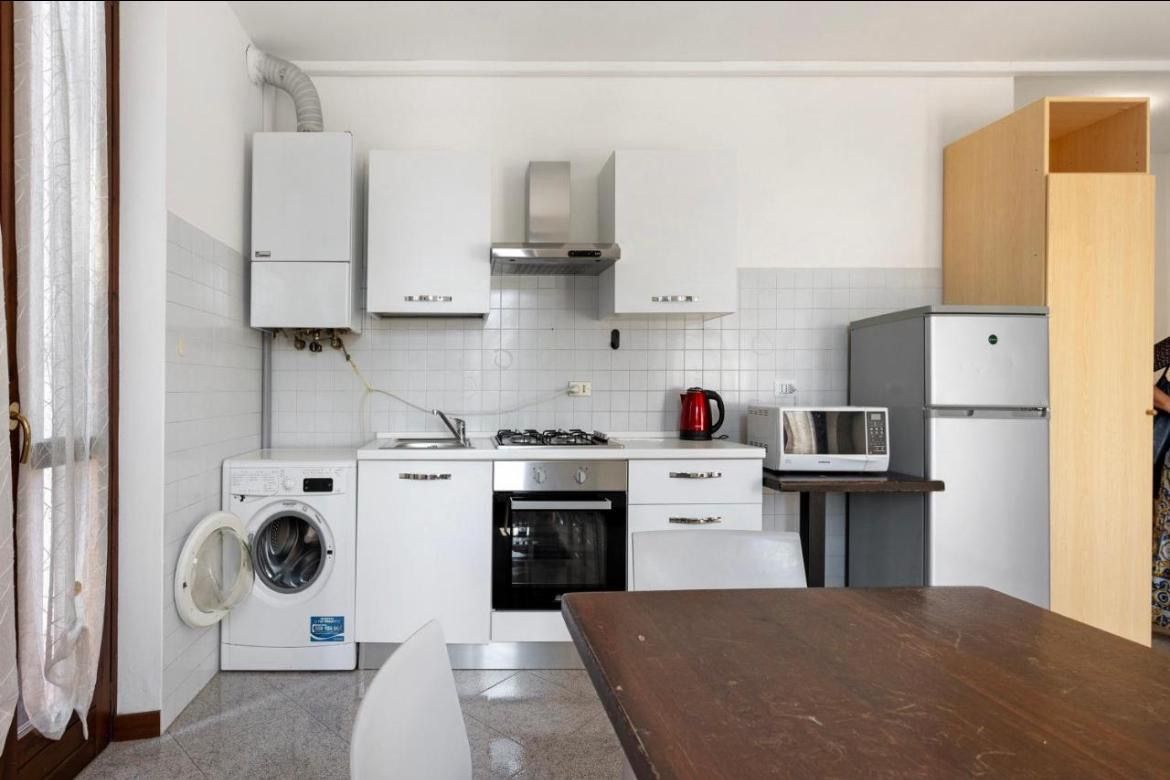 Een kleine keuken met een wasmachine, magnetron en een houten tafel.