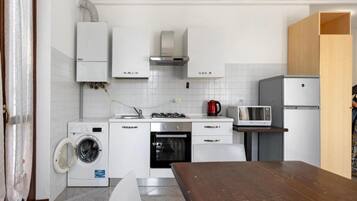 Een kleine keuken met een wasmachine, magnetron en een houten tafel.