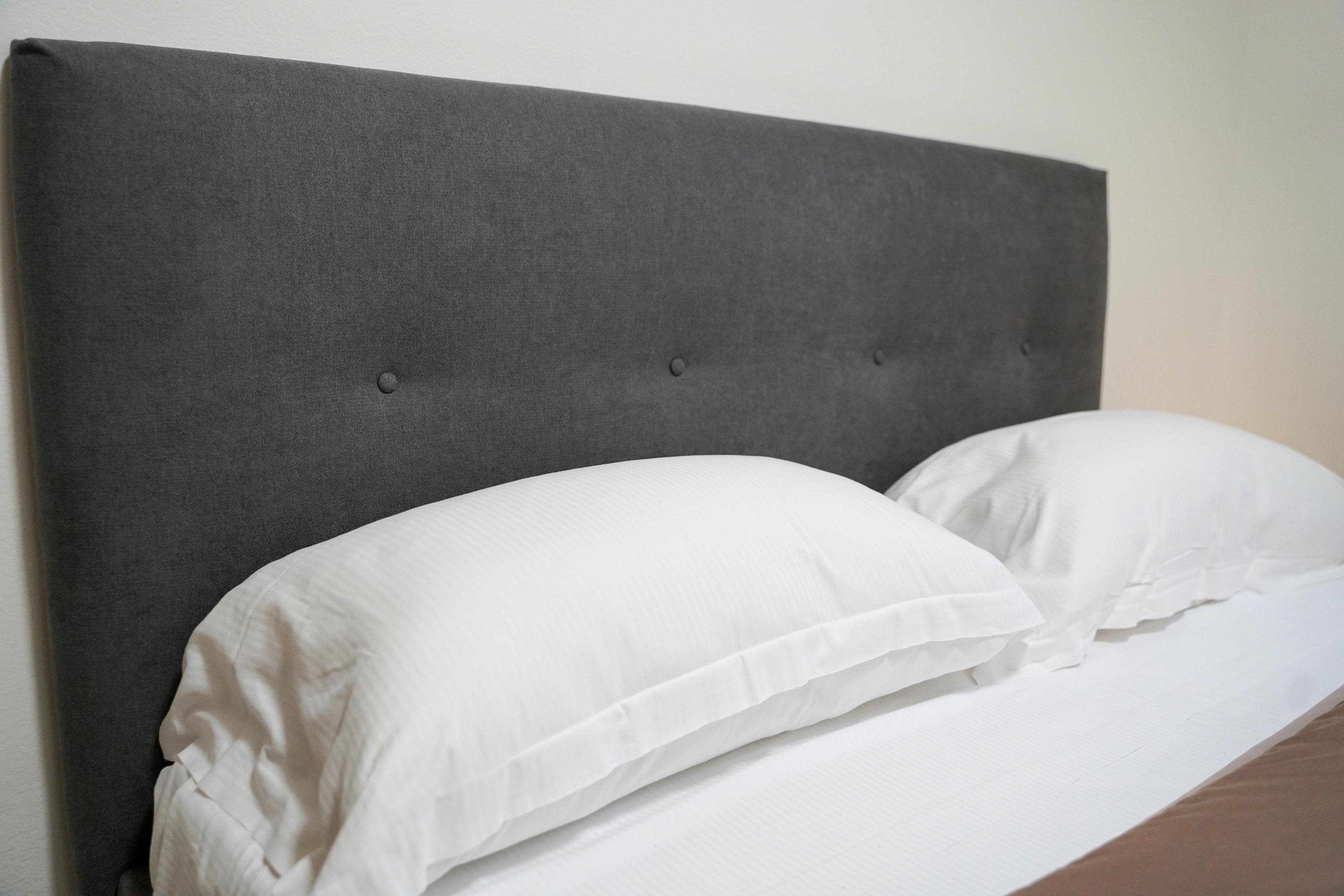 Ein Bett mit grauem Polsterkopfteil und weißen Kissen.
