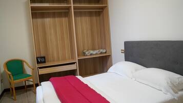 A bedroom with a bed, a wooden wardrobe, a chair, and a bedside table.