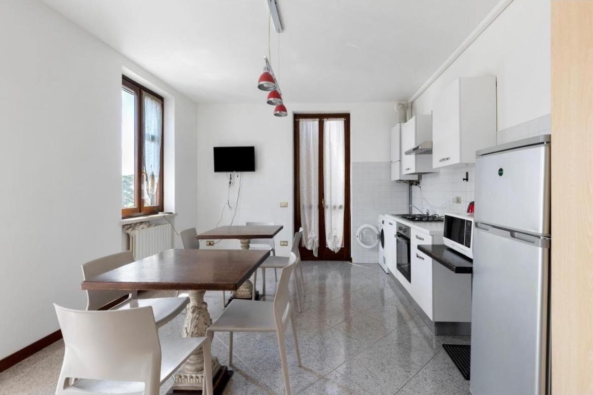 A compact kitchen with a dining table, chairs, a TV mounted on the wall, and modern appliances.