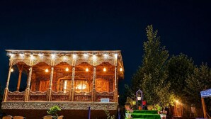 A building with ornate architecture, a staircase leading to a green lawn, and outdoor seating with tables and chairs. - De - Laila Group Of House Boats (Srinagar)