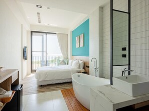 A modern bedroom with a large bed, a separate bathroom with a bathtub, and a balcony with a view. - Seawall Inn (Hengchun)