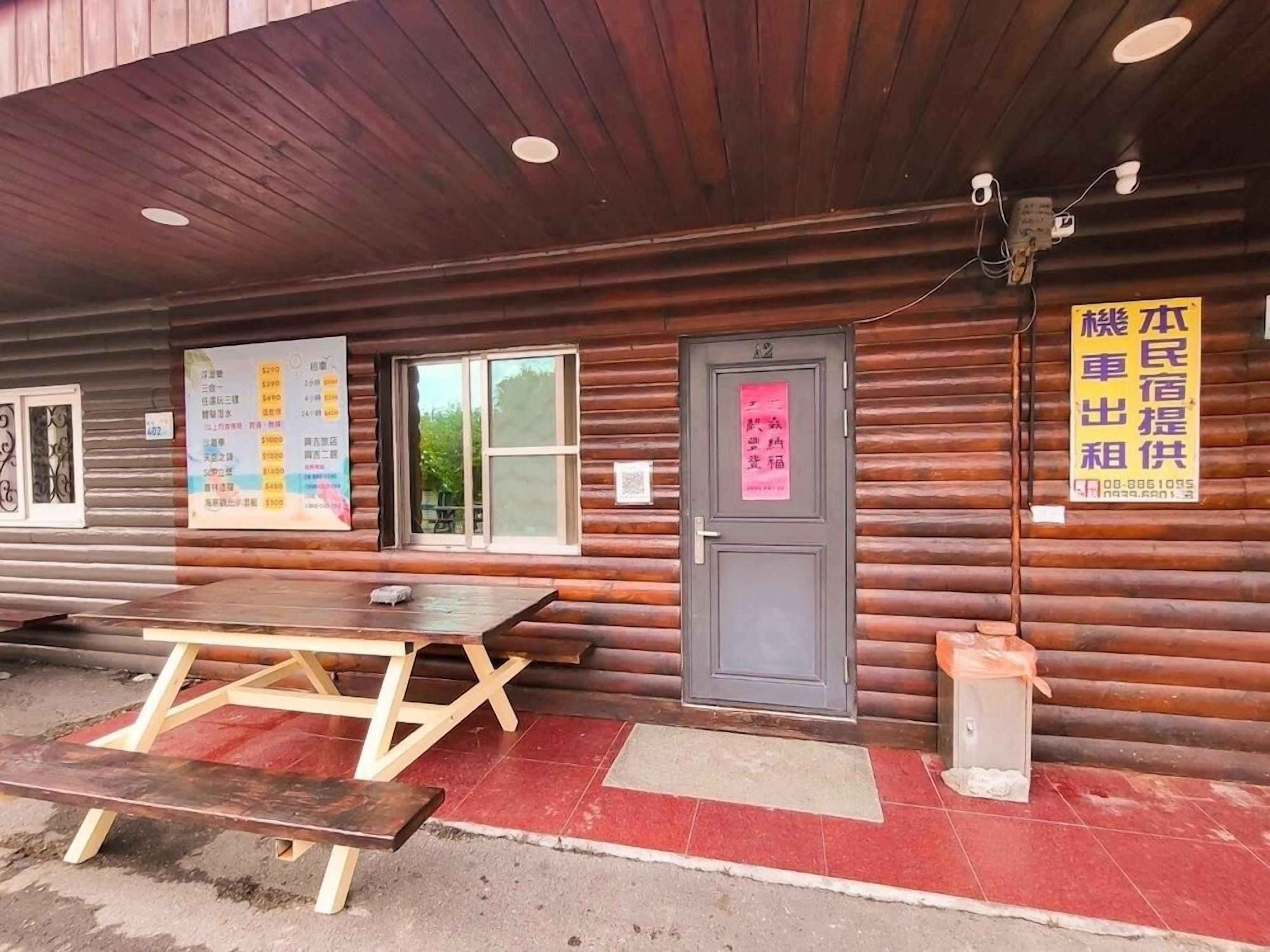 A wooden cabin with a picnic table, a door with a sign, and a menu board outside.
