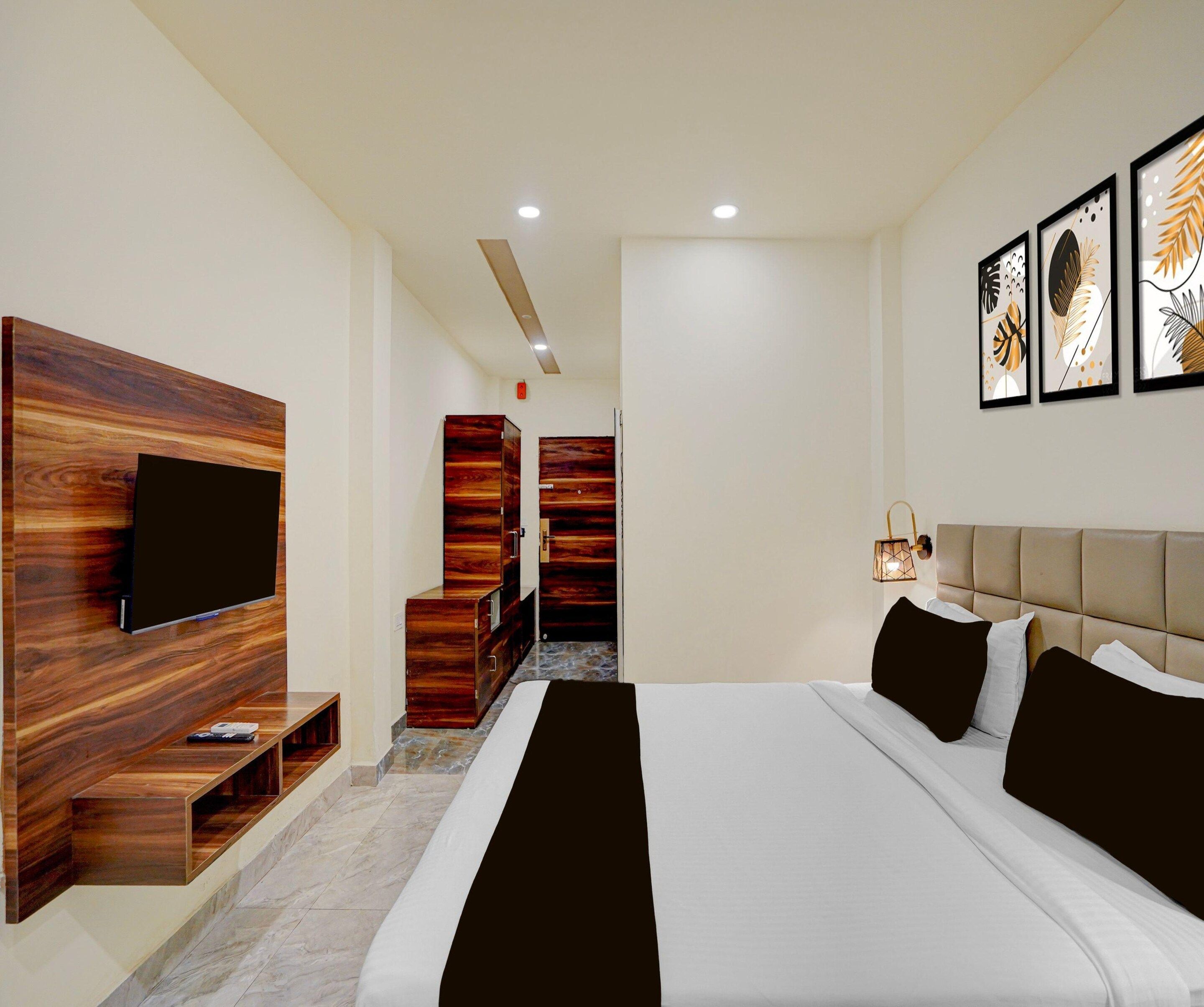 A modern hotel room with a large bed, a flat-screen TV mounted on a wooden panel, a wardrobe, and a bedside table.