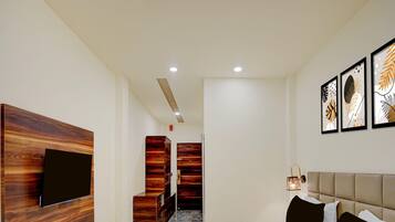 A modern hotel room with a large bed, a flat-screen TV mounted on a wooden panel, a wardrobe, and a bedside table.