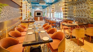 A restaurant with a long communal table, individual booths, and a patterned wall. - Family Rooms With Twin King bed Amar Resorrt (Motihari)