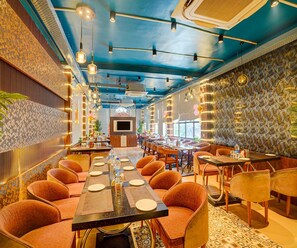 A restaurant with a long communal table, individual booths, and a patterned wall. - Family Rooms With Twin King bed Amar Resorrt (Motihari)