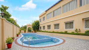 A swimming pool with a tiled deck, surrounded by a building with multiple windows and a gated entrance. - Family Rooms With Twin King bed Amar Resorrt (Motihari)