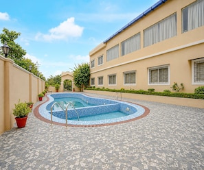 A swimming pool with a tiled deck, surrounded by a building with multiple windows and a gated entrance. - Family Rooms With Twin King bed Amar Resorrt (Motihari)