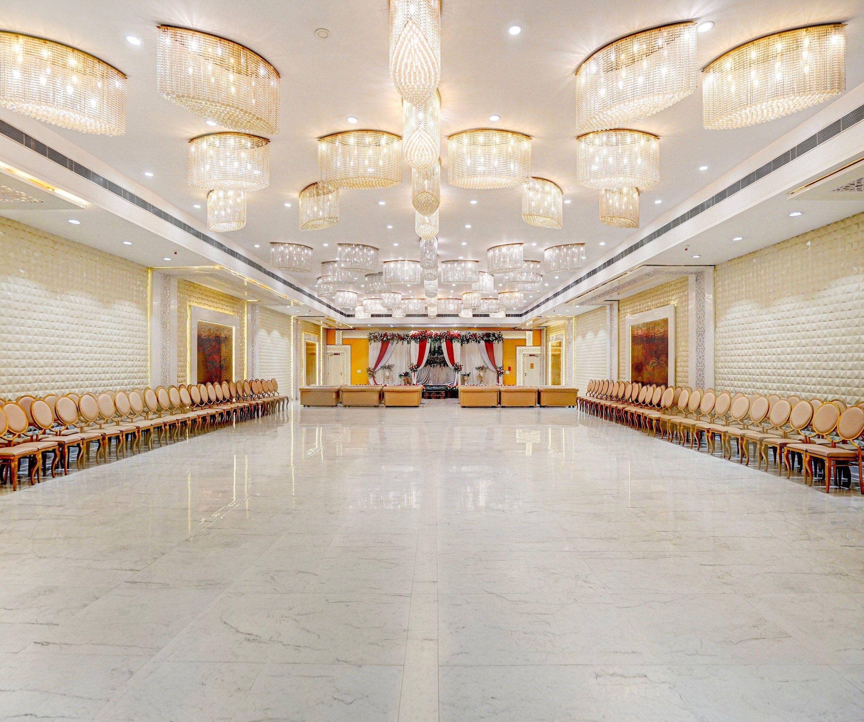 Un amplio salón con filas de sillas y un escenario frontal, decorado con candelabros y arreglos florales.