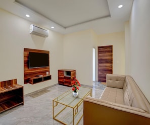 A modern living room with a flat-screen TV, wooden furniture, a glass coffee table, and a sofa.