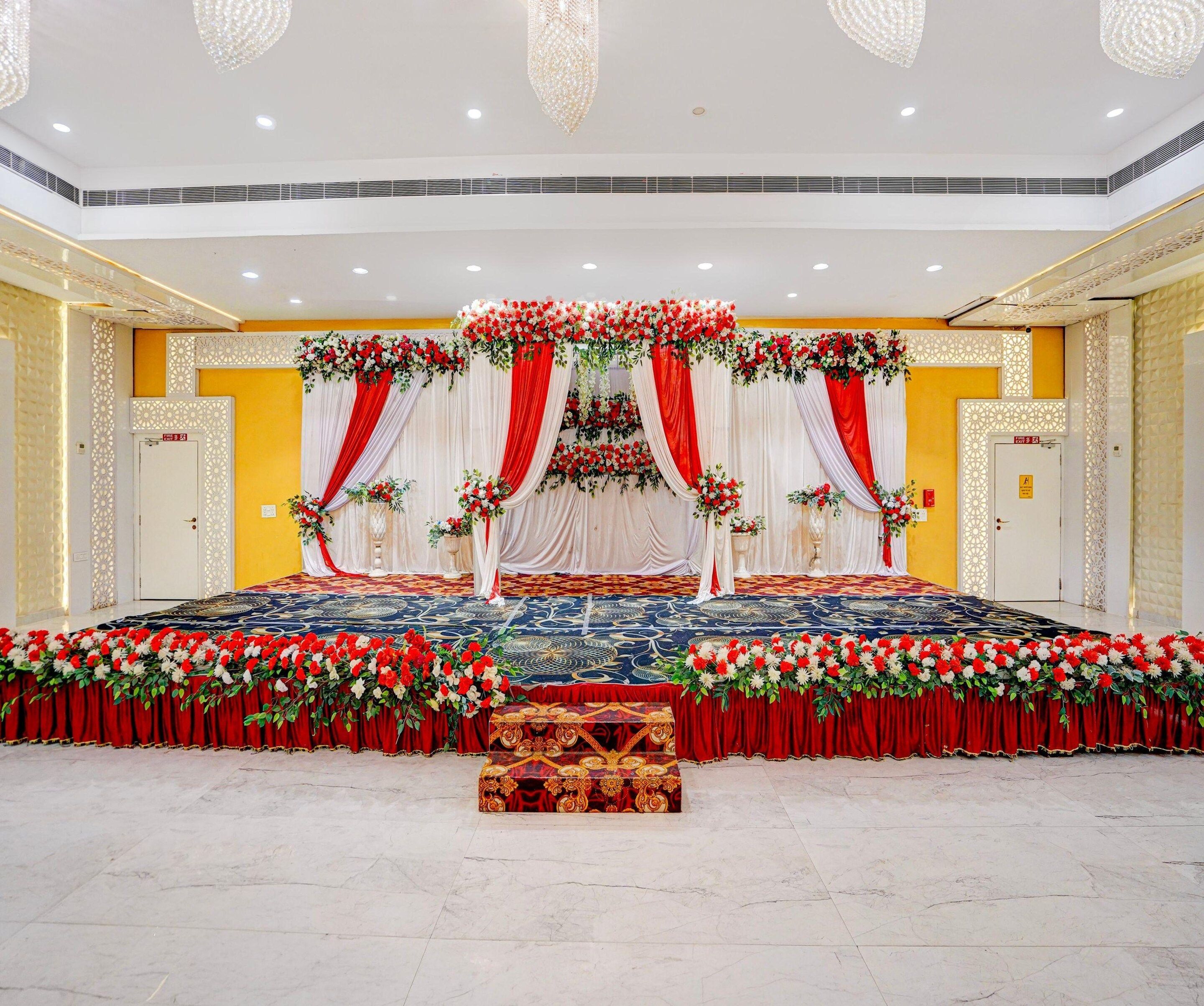 A stage with red and white drapes, floral arrangements, and a patterned carpet.