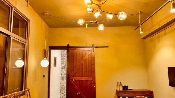 A hotel room with a bed, a desk, a chair, a wooden door, and a ceiling light fixture. - Loft.wo Design Inn (Tainan)
