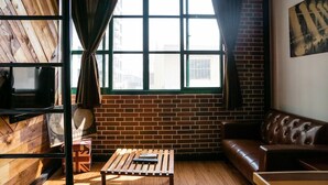A room with a brick wall, a wooden floor, a leather sofa, a wooden coffee table, and a large window with curtains. - Loft.wo Design Inn (Tainan)