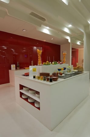 A modern kitchen with a white countertop, red cabinetry, and various food items displayed. - Keys Hotel (Thiruvananthapuram)