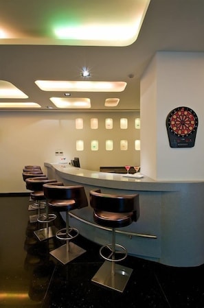 A bar area with a curved counter, multiple stools, and a dartboard on the wall. - Keys Hotel (Thiruvananthapuram)