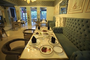 A dining area with a long table set for a meal, surrounded by upholstered chairs and a tufted sofa. - The Royal Retreat (Udaipur)