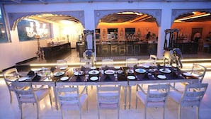 Uma sala de jantar com uma mesa comprida posta para vários convidados, rodeada por cadeiras ornamentadas.
