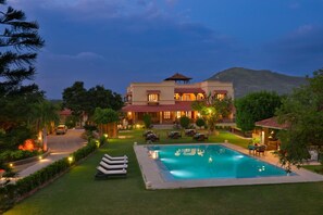 Un hotel con piscina, zona de estar al aire libre y montañas al fondo.