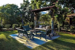 An outdoor patio with a table and chairs, surrounded by lush greenery and a pergola structure. - The Royal Retreat (Udaipur)