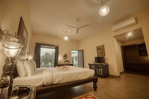 A bedroom with a bed, a ceiling fan, an air conditioning unit, a television, and a window with a view. - The Royal Retreat (Udaipur)