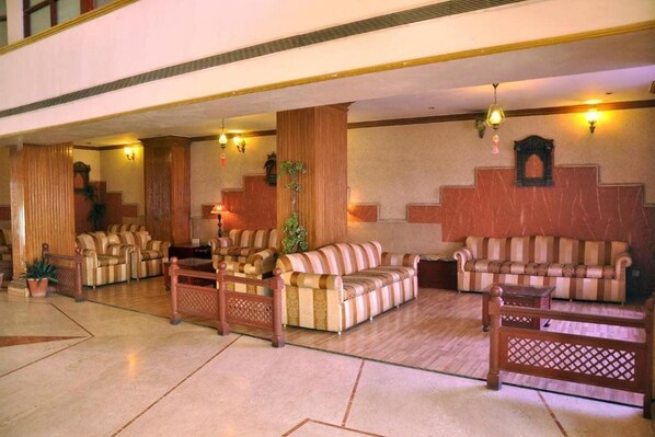 A lobby with multiple seating areas, including sofas and armchairs, arranged around a central column. - Ecko Premier Vibrant (Udaipur)