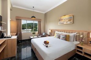 A hotel room with a large bed, a desk, a chair, a small table, and a window with curtains. - Ecko Premier Vibrant (Udaipur)