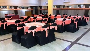 A banquet hall with round tables and chairs, some with pink sashes. - Ecko Premier Vibrant (Udaipur)