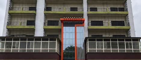 A multi-story building with a central entrance, balconies, and a reflective glass facade.