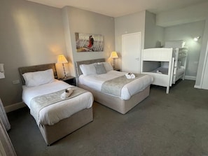 Una habitación de hotel con dos camas, una litera, un cuadro en la pared y una puerta.