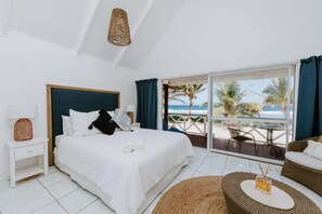 A hotel room with a bed, a nightstand, a wicker lamp, a view of the beach, and a balcony with a table and chairs.