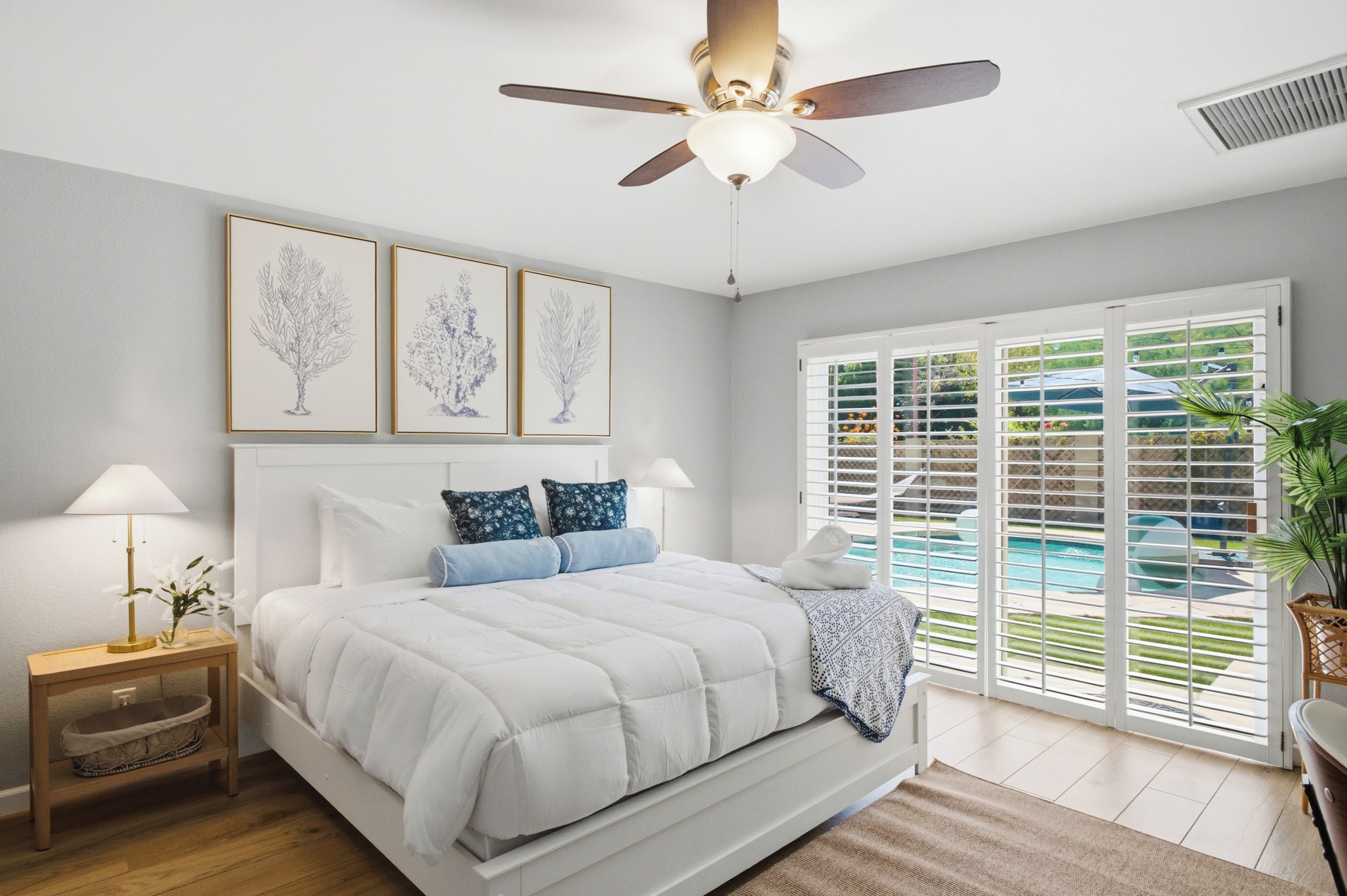 Un dormitorio con cama, mesitas de noche, ventilador de techo y vistas a una piscina a través de amplios ventanales.