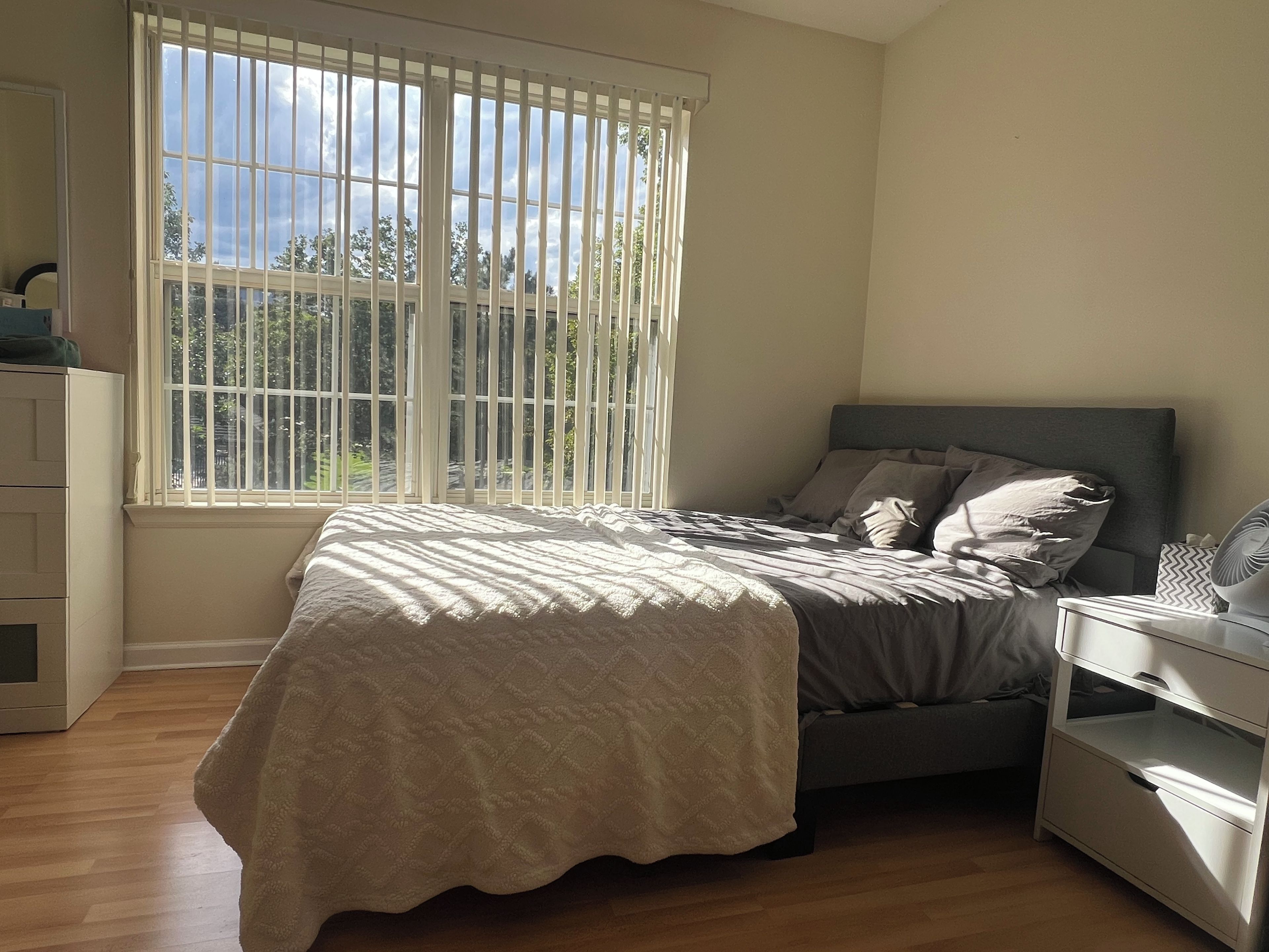 Une chambre à coucher comprenant un lit, une table de chevet, une commode et une fenêtre avec des stores.