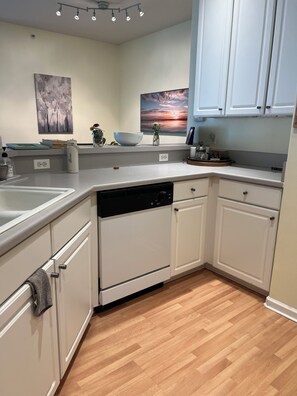 A modern kitchen with white cabinets, a dishwasher, and a countertop with various items. - Beautiful 2-bedroom condo in Boulder with fitness room, club house, pool, and AC (Boulder)