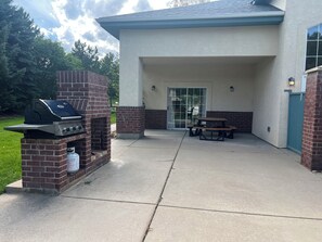 An outdoor patio with a brick barbecue grill, a picnic table, and a covered entrance. - Beautiful 2-bedroom condo in Boulder with fitness room, club house, pool, and AC (Boulder)