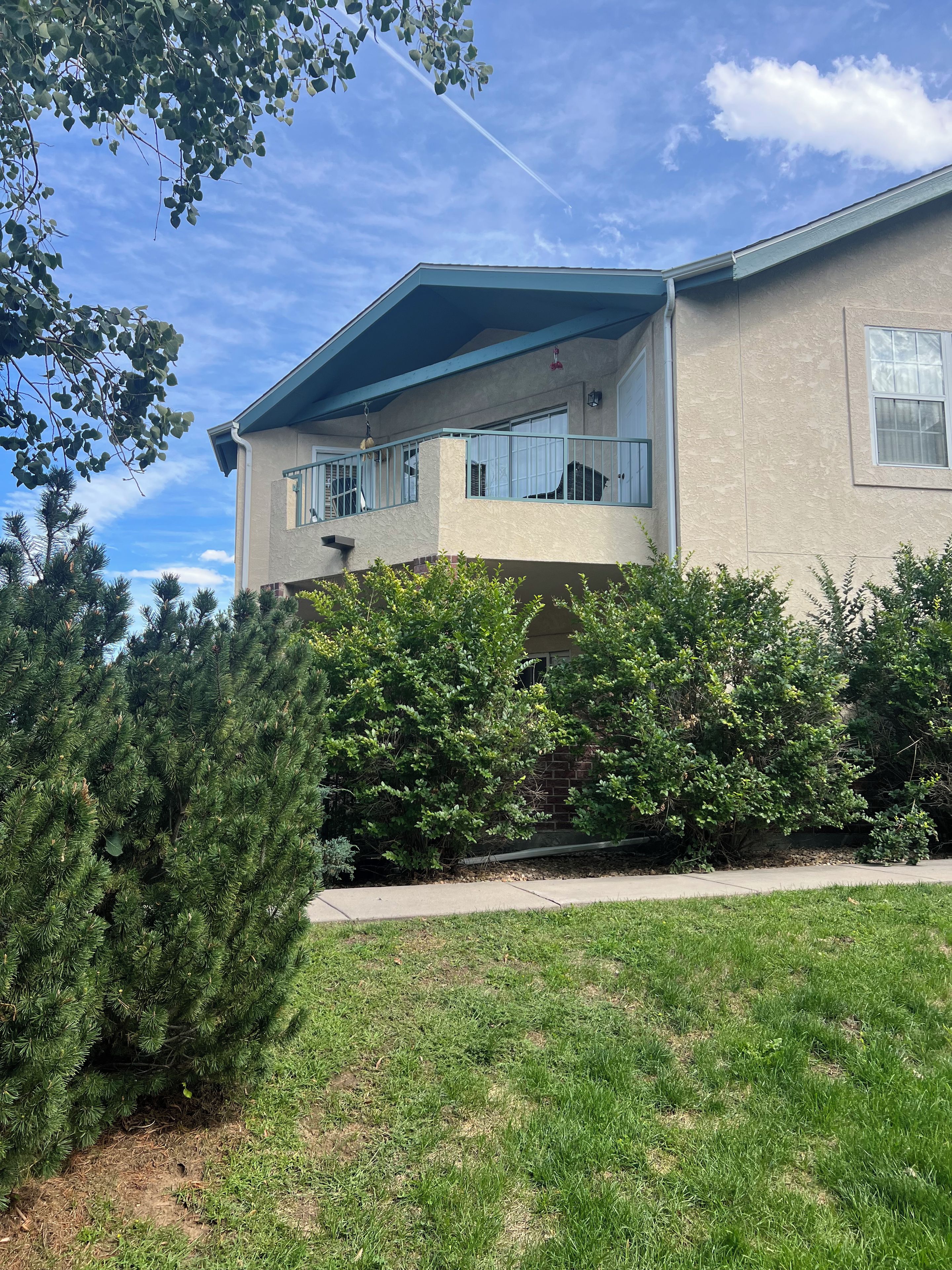 A two-story house with a covered balcony, a brick wall, and a grassy yard.