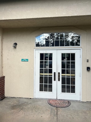 A double door with a small window above it, a brick wall to the left, and a sign indicating operating hours. - Beautiful 2-bedroom condo in Boulder with fitness room, club house, pool, and AC (Boulder)