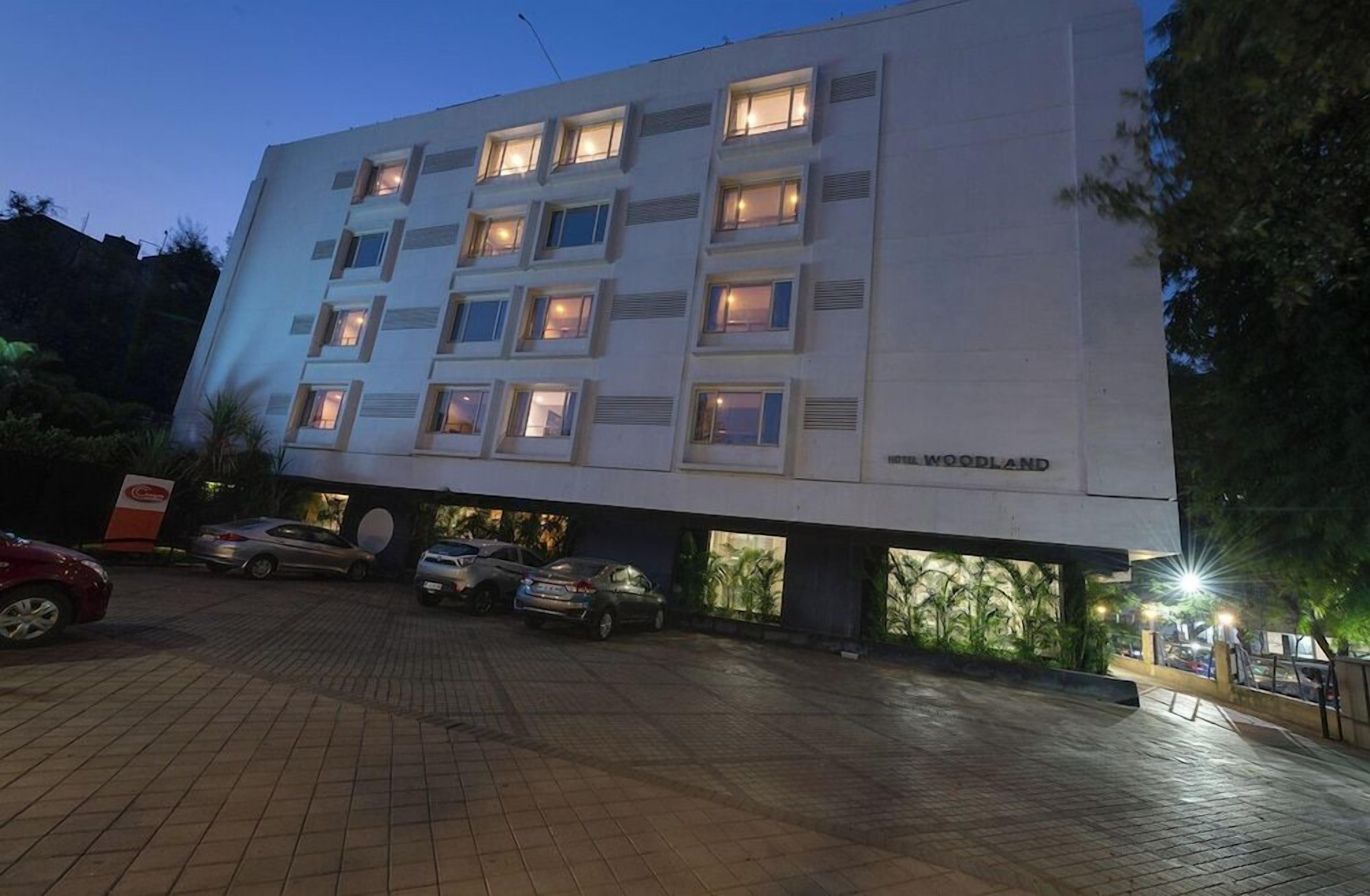 A multi-story hotel building with illuminated windows and a sign reading 'WOODLAND' at the bottom.