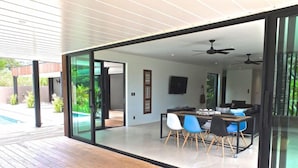 Uma área de refeições moderna com porta de vidro que dá para um espaço ao ar livre, ventilador de teto e TV de tela plana.