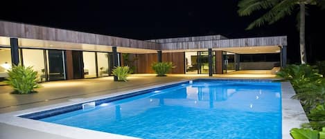 Una casa moderna con piscina, puertas de vidrio e iluminación exterior.